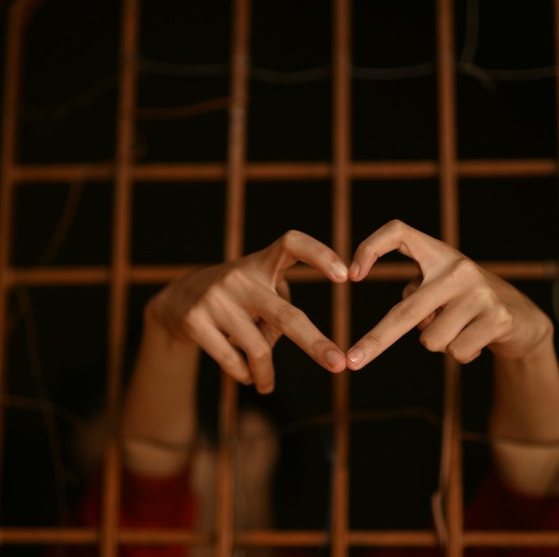 Manos formando un corazón detrás de barrotes, símbolo de los mandatos familiares que limitan la libertad y afectan la salud mental